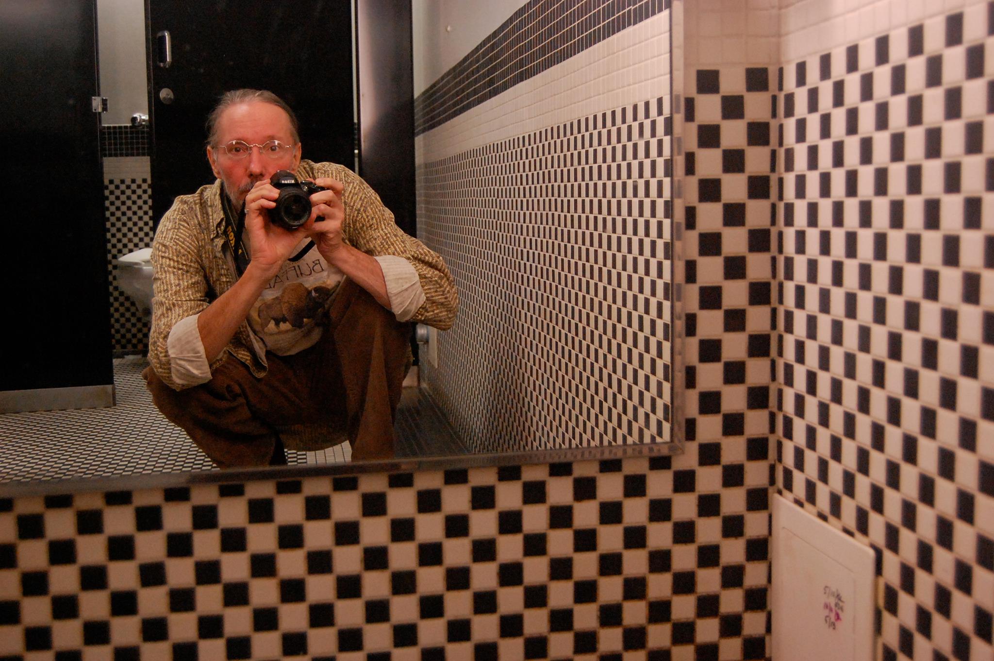 Photographer self-portrait in the mirror of a bathroom with checkered tiles