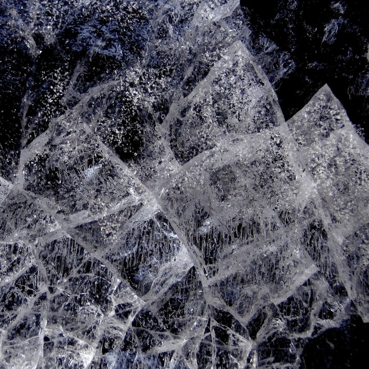 Thick sheet of ice with crosshatched crack patterns against a dark background