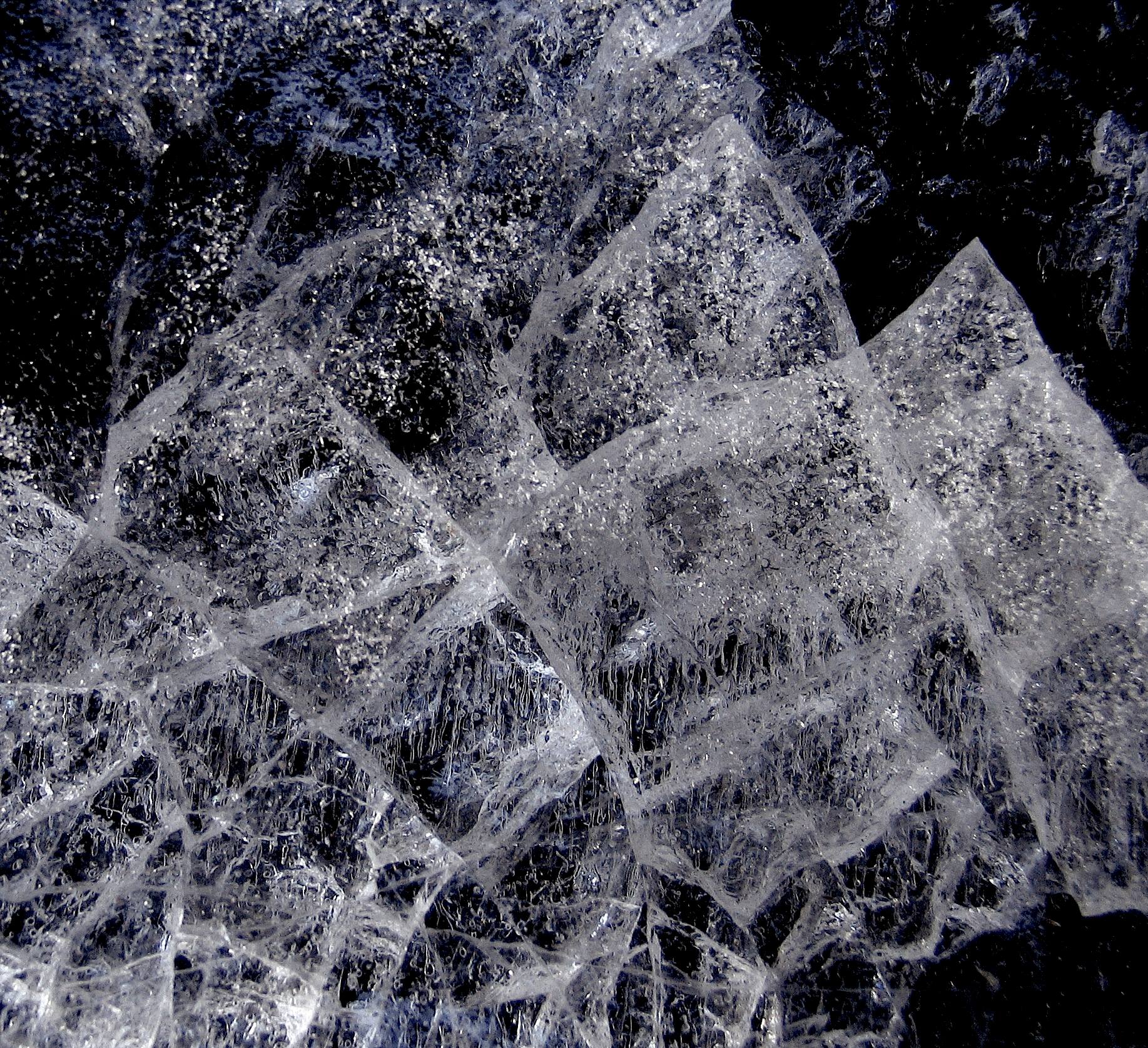 Thick sheet of ice with crosshatched crack patterns against a dark background