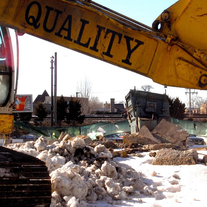 Shovel loader boom with the word QUALITY painted on it, framing a construction landscape.
