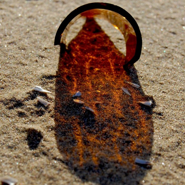 Sun filtering through the brown glass of a broken bottle onto sand