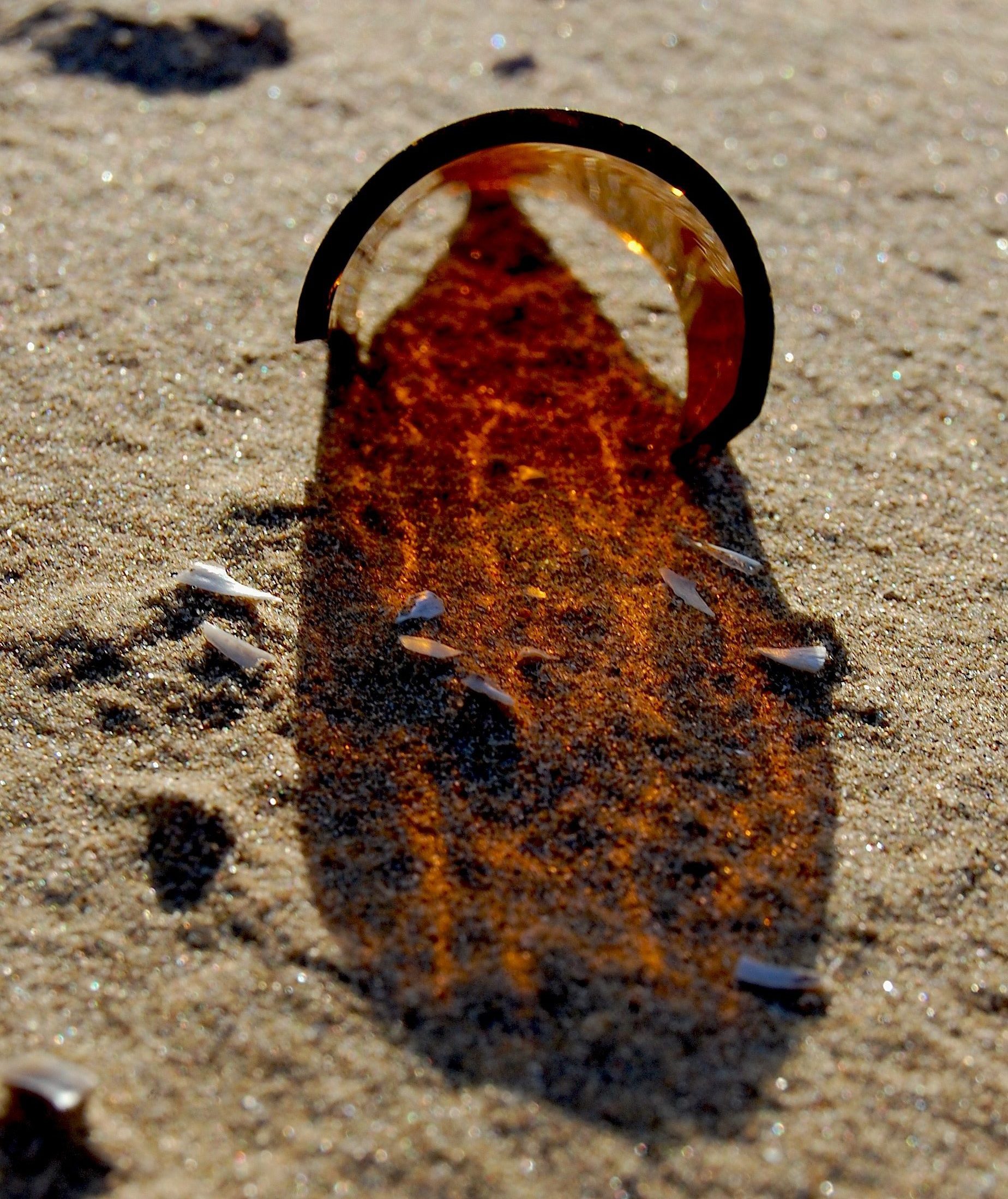 Sun filtering through the brown glass of a broken bottle onto sand
