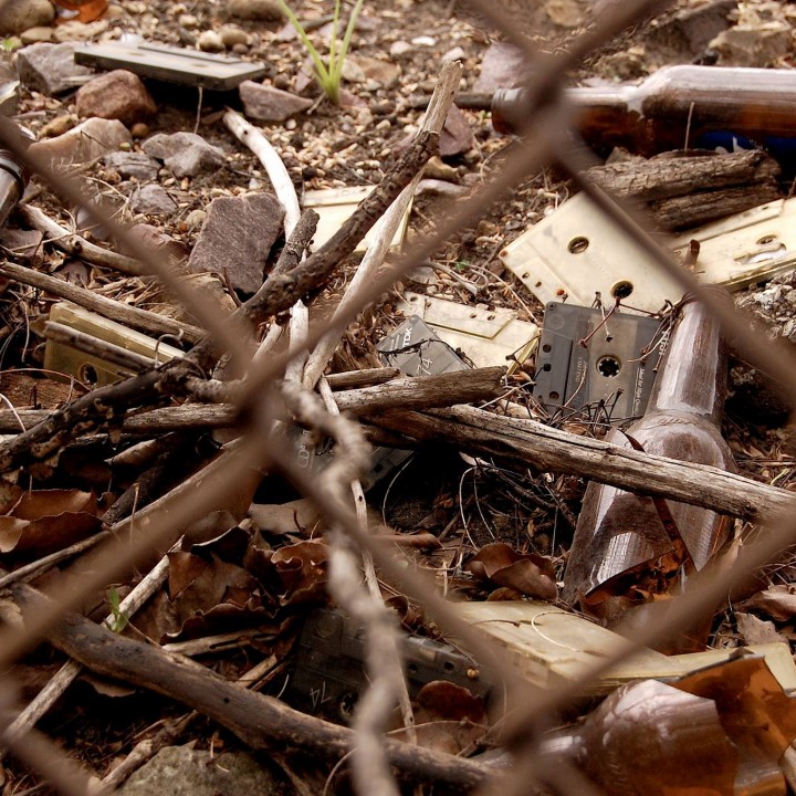 Cassettes and broken bottles on the ground behind a chain link fence