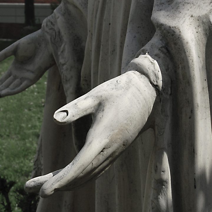 Hands of a statue of The Blessed Virgin Mary, one in light, one in shadow