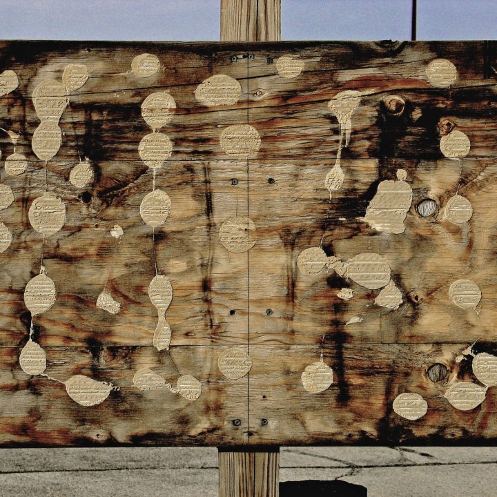 Sign in decay, building materials plywood and post remail in day-lit parking lot